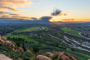 Altın gün batımı, Riverside, California, vadiyi aydınlatıyor. Canlı yeşil parklar ve kıvrımlı, kuru bir nehir yatağı sergileniyor. Hepsi görkemli Rubidoux Dağı patikasından..