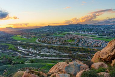 Yükseltilmiş perspektif, Riverside, California 'nın yayılan kentsel manzarasını gözler önüne seriyor. Güzel, altın saat gökyüzü altında canlı bir doğal araziye kurulmuş, ince aydınlatılmış bulutlarla..