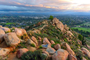 Geniş panoramik manzarada Rubidoux Dağı 'nın kayalık arazisi ön planda uzanan Riverside, California şehri alacakaranlık bulutlarının altında yer almaktadır..