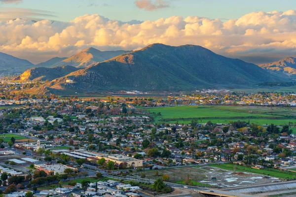 Kaliforniya 'daki Rubidoux Dağı Patikası' ndan dramatik bulutlu bir gökyüzünün altındaki yerleşim yerlerine ve sıradağlara bakan altın saat manzaralı nehir kenti..