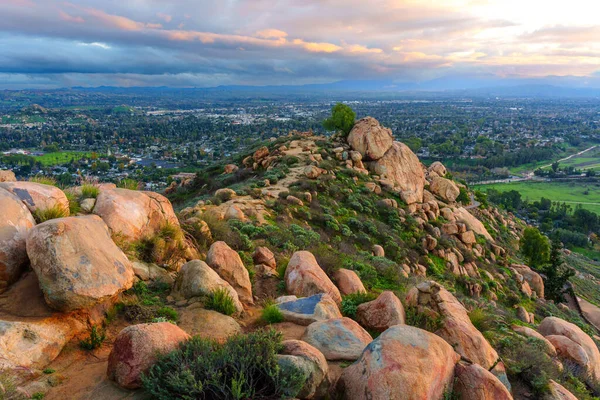 Geniş panoramik manzarada Rubidoux Dağı 'nın kayalık arazisi ön planda uzanan Riverside, California şehri alacakaranlık bulutlarının altında yer almaktadır..