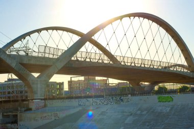 Los Angeles, Kaliforniya - 10 Ocak 2026: 6. Cadde Viaduct kemerleri ve asma kabloları Los Angeles Nehri yatağı boyunca uzanır ve arka planda şehir duvar yazıları ve şehir binaları bulunur..