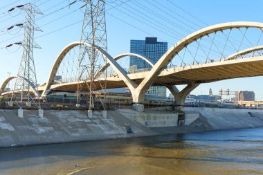 Los Angeles, Kaliforniya - 10 Ocak 2026: 6. Cadde Viaduct 'unun beton kemerleri Los Angeles Nehri boyunca uzanır, aşağıdaki Metrolink treni, belirgin elektrik hatları ve uzak bir şehir silueti yer alır..
