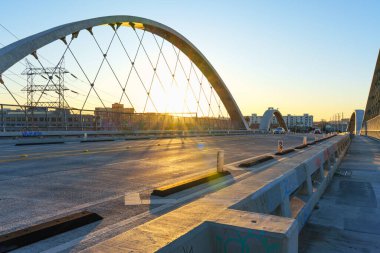 Los Angeles, Kaliforniya - 10 Ocak 2026: Altıncı Cadde Viaduct kemerleri batan güneşi çerçeveliyor, altın saat boyunca Los Angeles 'ta arabalarla yol boyunca sıcak ışık saçıyor.