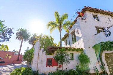 Beyaz sıva duvarlı parlak Santa Barbara binası, kırmızı aksanlı, yemyeşil, ve açık mavi gökyüzünün altında uzun palmiye ağaçları..