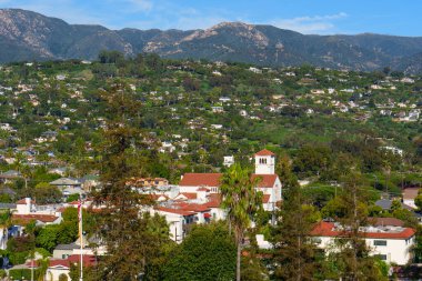 Yükselen manzara gösteriyor ki Santa Barbara 'nın yerleşim yerleri yemyeşil yamaçlara yayılmış, evlerle ve engebeli dağlara karşı önemli bir kiliseyle noktalanmış..
