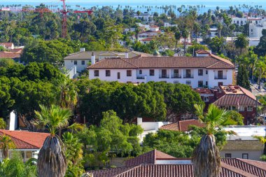 Ufuktaki parlak mavi Pasifik Okyanusu 'na doğru uzanan kırmızı kiremitli çatılar ve yoğun yeşilliklerle karakterize edilen Santa Barbara kentsel kumaşının kapsamlı hava görüntüsü.