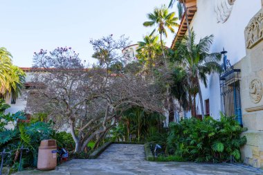 Santa Barbara, California - 29 Aralık 2025: Tarihi Santa Barbara İlçesi Avlusu açık mavi Kaliforniya gökyüzü altında yemyeşil, palmiye ağaçları ve taş yollar barındırıyor.