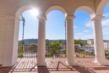 Santa Barbara, Kaliforniya - 29 Aralık 2025: Tarihi Santa Barbara balkonunda beyaz kemer ve kolonlar güneşli bir şehir manzarası, uzak yeşil tepeler ve açık mavi bir gökyüzü sunar..