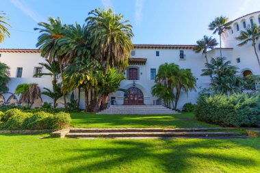Santa Barbara, California - 29 Aralık 2025: Kırmızı kiremit çatılı beyaz sıva bina ve büyük kemerli giriş merdivenleri canlı yeşil çimenler ve yükselen palmiye ağaçları arasında gururla duruyor.
