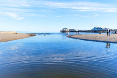 Santa Barbara, California - 29 Aralık 2025: Sakin bir haliçin okyanusla birleştiği sakin bir sahne, arkada ikonik Stearns Rıhtımı ve plajın keyfini çıkaran birkaç kişi.