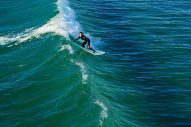 Okyanus Kenarı, Kaliforniya - 17 Aralık 2025: Okyanus kıyısındaki berrak sularda güçlü, zümrüt yeşili bir dalgaya ustalıkla binen bir sörfçünün aksiyon dolu görüntüleri. Ekstrem sporlar ve okyanus macera teması.
