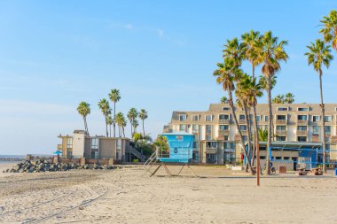 Okyanus Kenarı, Kaliforniya - 17 Aralık 2025: Okyanus Kıyısı manzaralı, mavi bir cankurtaran kulesi, yemyeşil palmiye ağaçları ve okyanus manzaralı oteller,.