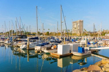 Okyanus Kenarı, Kaliforniya - 17 Aralık 2025: Okyanus Kıyısı 'nın dinamik görüntüleri, açık mavi gökyüzü altında modern kıyı binalarının zeminine kurulmuş yelkenliler ve yatlarla dolu.