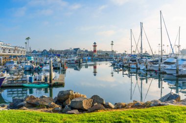 Okyanus Kenarı, Kaliforniya - 17 Aralık 2025: Geniş, sakin, yansıtıcı sular, merkezi bir kırmızı ve beyaz deniz feneri ve kenetlenmiş çok sayıda tekne sergilenmektedir..