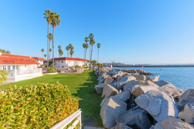 Kırmızı çatıları, yeşil çimenleri ve palmiyeleri olan beyaz binalar mavi Pasifik Okyanusu 'nun yanında bir kaya iskelesi gibi uzanır..