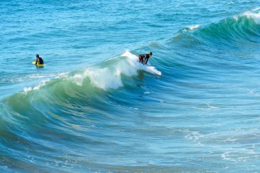 Okyanus Kenarı, Kaliforniya - 28 Aralık 2025: Sörfçü, parlak bir günde okyanus kıyısında dalgalanan mavi-yeşil bir okyanus dalgasına ustaca biniyor..