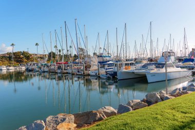 Okyanus Kenarı, Kaliforniya - 28 Aralık 2025: Okyanus kıyısında çeşitli yat ve yelkenlilerle dolu, parlak mavi bir gökyüzünün altında yansımaları parlıyor..