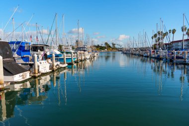 Oceanside, California - 28 Aralık 2025: Oceanside Marina 'nın ana kanalı boyunca çeşitli tekneler ve sakin mavi sudaki ayna benzeri yansımaları ile çevrili sakin bir manzara.