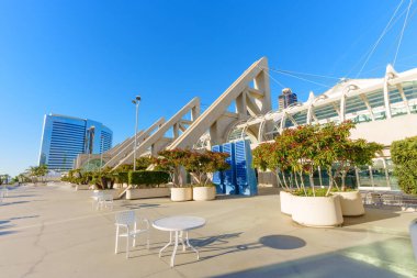 San Diego Kongre Merkezi 'nin modern mimarisi açık mavi gökyüzünün altında, açık hava oturma alanları, saksı bitkileri ve şehir gökdelenleri barındırıyor..