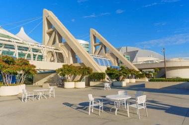 San Diego Kongre Merkezi, beyaz bahçe mobilyaları ve yemyeşil yeşillik içeren temiz bir terasın üzerinde ikonik mimari destekleri ve cam çatıyı sergiliyor..