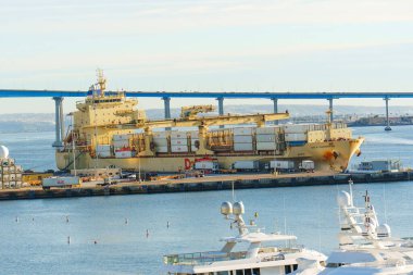 San Diego, California - 30 Aralık 2025: San Diego 'nun aktif limanında sanayi vinçleri, diğer gemiler ve arka planda ikonik Coronado Köprüsü bulunan büyük bir konteyner gemisi yanaştı.