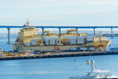 San Diego, California - 30 Aralık 2025 San Diego 'nun hareketli limanına demirlemiş olan Dole Karayip konteynır gemisinin kargosunun Coronado Köprüsü' ne doğru yüklendiği ayrıntılı görüntüsü.