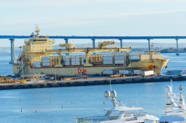 San Diego, California - 30 Aralık 2025: Massive Dole Karayip konteynır gemisi San Diego 'nun işlek limanına yanaştı, konteynırlarla dolu, lüks yatların yanında ve ikonik Coronado Köprüsü.