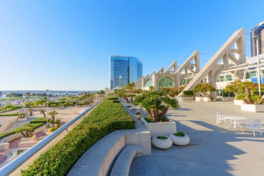 San Diego, California - 30 Aralık 2025: San Diego Kongre Merkezi terasında açık mavi gökyüzü altında modern mimari, canlı peyzaj ve hareketli bir marina yer almaktadır..
