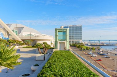 San Diego, California - 30 Aralık 2025: Camdan asansör ve yemyeşil bitkilerle modern kongre merkezi, bir sokağa, körfeze ve uzak Coronado Köprüsü 'ne bakıyor..