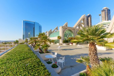 San Diego, California - 30 Aralık 2025: Kongre merkezi terasında modern mimari, beyaz veranda oturma, yeşil palmiye ağaçları ve arka planda yansıtıcı bir gökdelen bulunan açık bir gökyüzü yer almaktadır..