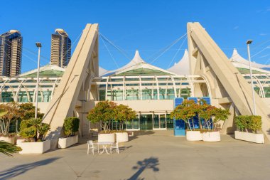 San Diego, California - 30 Aralık 2025: San Diego Kongre Merkezi 'nin beyaz çadırlı çatısı ve cam ön cephesi açık mavi gökyüzüne karşı, yeşil bitkiler ve uzak şehir kuleleriyle tamamlanmış.