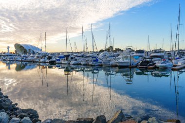 San Diego, California - 30 Aralık 2025: San Diego, Kaliforniya 'da canlı bir marinaya demirlemiş çok sayıda tekne, günbatımında gökyüzünün renklerinin durgun sulara güzel yansımasıyla.