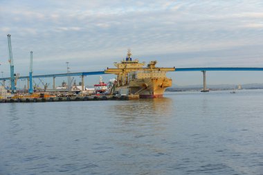 San Diego, California - 30 Aralık 2025: Büyük kargo gemisi San Diego limanına demirlemiş, etkileyici Coronado Köprüsü bulutlu bir gökyüzünün altında uzanmaktadır..