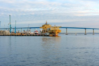 San Diego, California - 30 Aralık 2025: Limanda bir kargo gemisi, limanda endüstriyel vinçler ve ikonik Coronado Köprüsü 'nün yer aldığı geniş bir manzara.