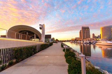 San Diego, California - 30 Aralık 2025: San Diego 'da sahnelenen sahil yürüyüşü, şehrin ufuk çizgisi, marina ve Rady Shell manzarasını renkli bir günbatımı altında sunuyor..