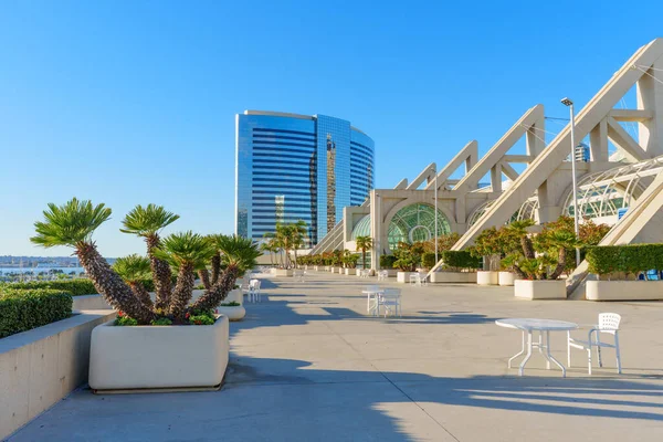San Diego, California - 30 Aralık 2025: San Diego Kongre Merkezi 'ndeki geniş ve güneşli açık hava terasında palmiye benzeri bitkileri olan beyaz veranda oturma yerleri ve sanatsal ekiciler yer alıyor..
