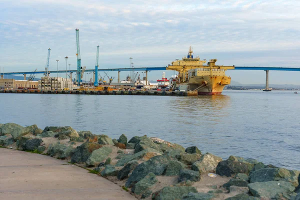 San Diego, California - 30 Aralık 2025: San Diego 'daki hareketli sanayi limanında bir kargo gemisi, yüksek vinçler ve sakin körfez boyunca uzanan ikonik Coronado Köprüsü bulunuyor..