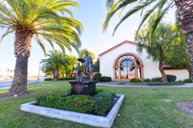 Perris, California - 6 Aralık 2025: Cesar E. Chavez Kütüphanesi ve palmiye ağaçları ve yeşil çimlerle çevrili bronz heykel Perris, Kaliforniya 'da açık mavi bir gökyüzü altında.