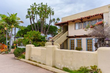 San Diego, Kaliforniya - 30 Aralık 2025: San Diego, Kaliforniya 'da bulunan tarihi İspanyol Koloni Uyanış binası, bronz sıva duvarları, kırmızı kil kiremit çatı, açık merdivenler ve tropikal palmiye ağaçları.