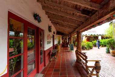 San Diego, California - 31 Aralık 2025: İspanyol sömürgesi kapaklı yürüyüş yolu, kırmızı fayanslı zemin ve ahşap kirişlerle, yemyeşil bitkiler ve büyüleyici dükkanların yer aldığı canlı bir avluya çıkıyor..