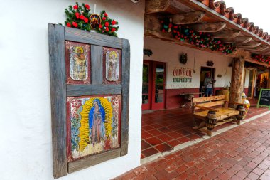 San Diego, California - 31 Aralık 2025: Meryem Ana ve azizlerin yer aldığı süslü dini panel, İspanya 'nın Zeytinyağı Mağazası' nın koloni mimarisini tamamlayan beyaz bir sıva duvarı süsler..