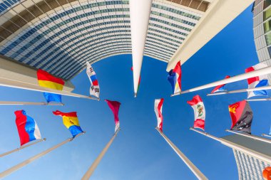 Viyana, Avusturya - 26 Şubat 2026: Ulusal bayraklar Viyana Uluslararası Merkezi 'nde açık mavi gökyüzü ve modern eğri mimari yapı cephesine karşı dalgalanıyor.