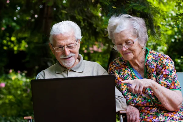 Elderly couple having fun with the laptop outdoors 图库图片