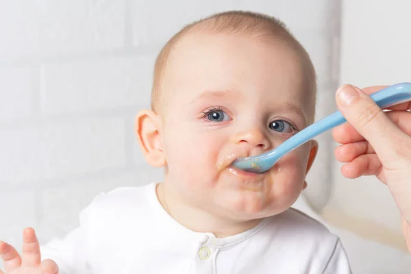 Mother feeding baby with blue baby spoon.