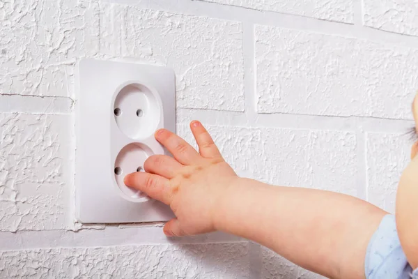 Elektrik prizinin yanında küçük bir el var. Tanınmayan beyaz erkek bebek Avrupa 'nın açık elektrik priziyle oynuyor. Yakın plan..