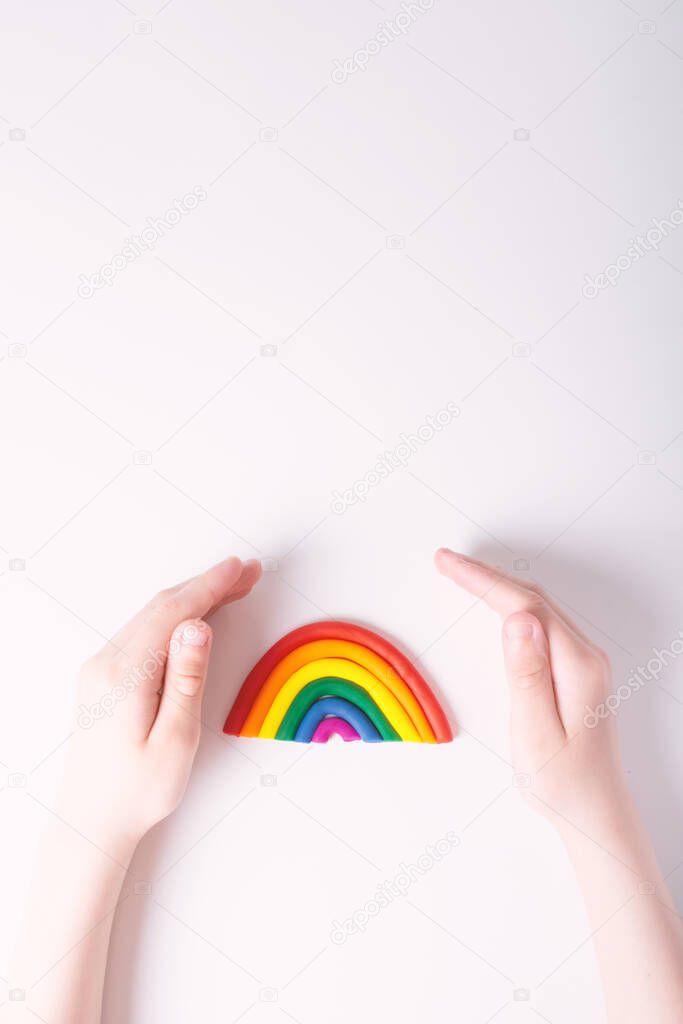 KId's hands around plasticine rainbow. LGBT family concept. Top view. Colors of gay flag. Light background. Copy space on top.