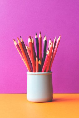 Colored pencils of purple and pink tint in ceramic holder in front of the background of trendy minimalistic colors.