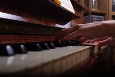 Beyaz bir kız evde piyano çalıyor. Seçici odaklanma. Önplanda mavi beyaz ve siyah piyano tuşları. 