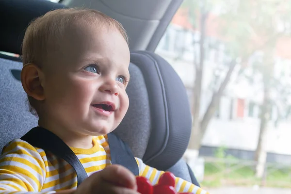 Szczęśliwe dziecko siedzi w foteliku samochodowym, bawiąc się. — Zdjęcie stockowe
